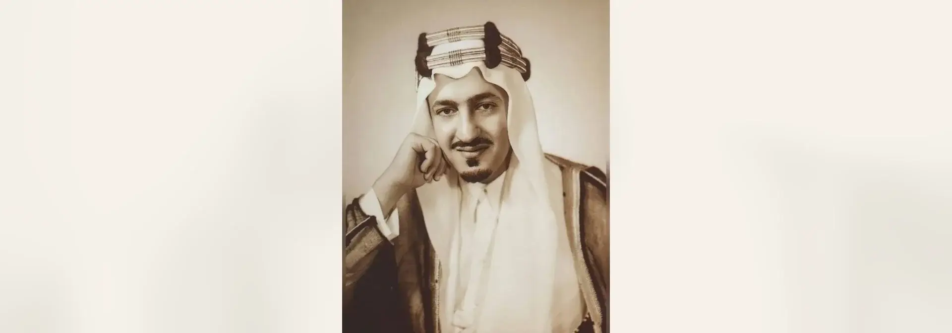 بورتريه تاريخي بالأبيض والأسود بمسحة سيبيا للأمير عبدالله الفيصل بن عبدالعزيز آل سعود، شابّ بشارب ولحية خفيفة يلبس غترة وعقالاً بكرات صوفية سوداء وبشتاً بحاشية مذهّبة، ويده على ذقنه أمام خلفية استوديو فاتحة