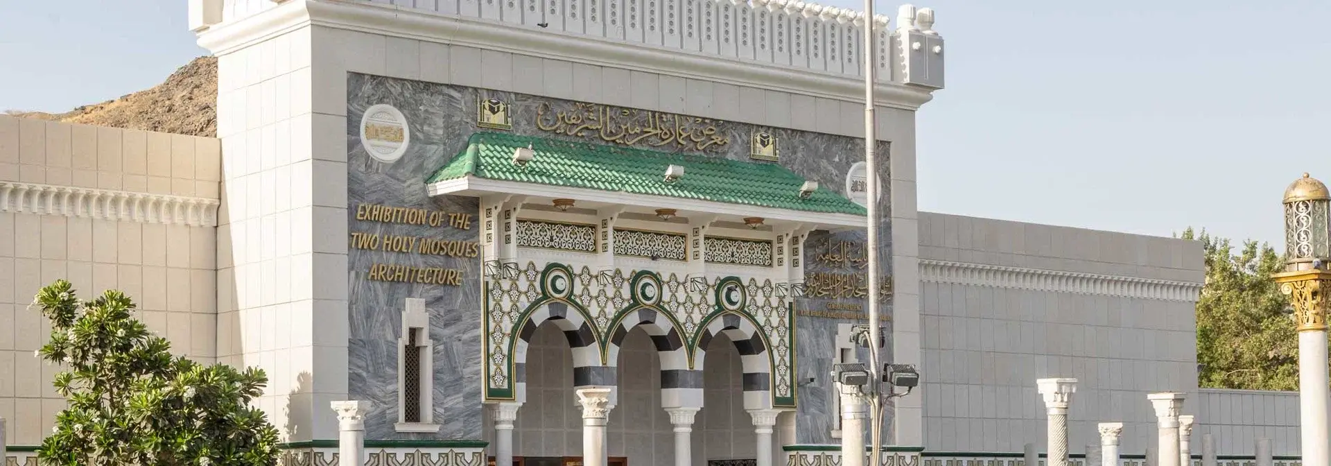 The entrance façade of the Exhibition of the Architecture of the Two Holy Mosques in Makkah, with marble arches, a green canopy and the exhibition's name inscribed in Arabic and English