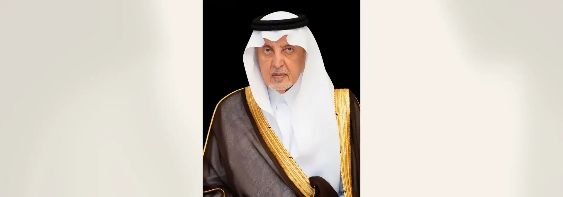بورتريه رسمي للأمير خالد الفيصل بغترة بيضاء وعقال أسود وبشت بنقشة ذهبية على خلفية داكنة