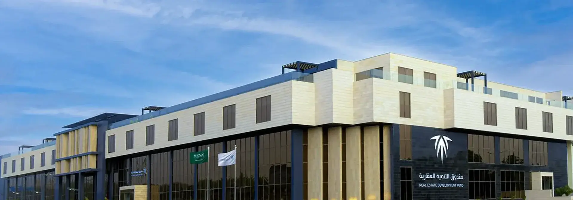مبنى صندوق التنمية العقارية في مدينة الرياض بواجهته الحجرية الفاتحة وزجاجه الداكن وشعار السعف ولوحة الاسم بالعربية والإنجليزية