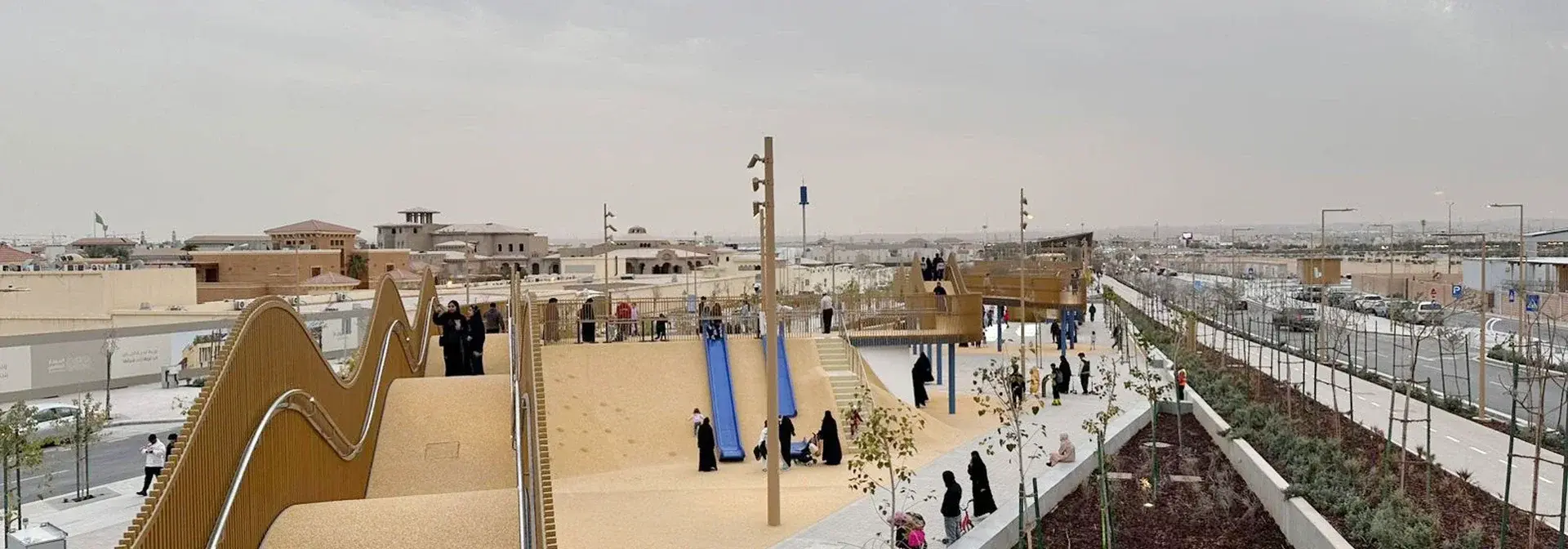 The golden wave-shaped Promenade walkway of the Sports Boulevard in Riyadh, with footpaths, slides and visitors amid newly planted trees
